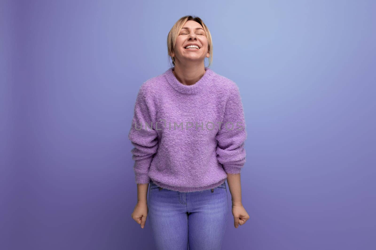 portrait of a joyful cute blondie woman in a lavender sweater on a purple background with copy space.