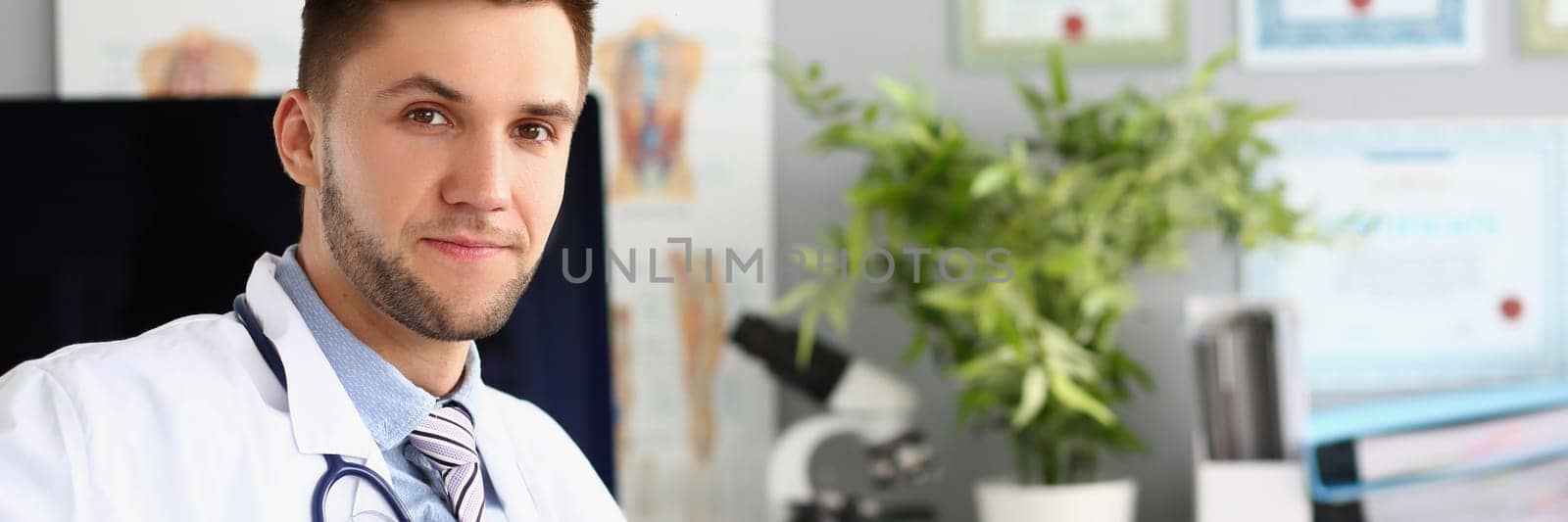 Portrait of young doctor sits in clinic office. Medical services insurance and examination in hospital