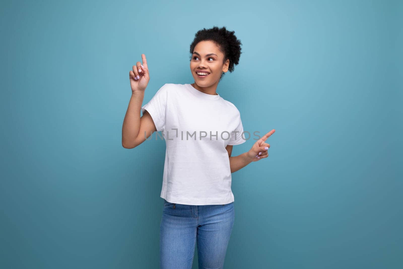 pretty young brunette hispanic woman in a white t-shirt shows with her hands on an empty space for advertising by TRMK