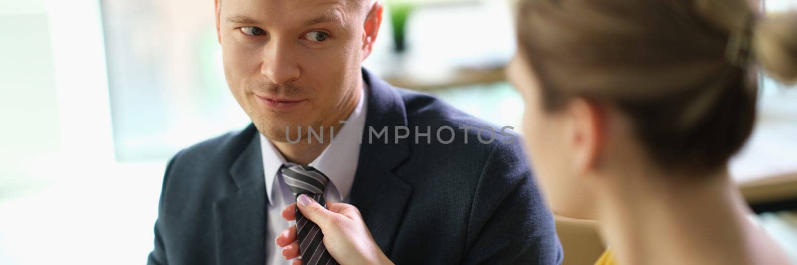 Woman secretary straightening tie to manager man at work in office by kuprevich