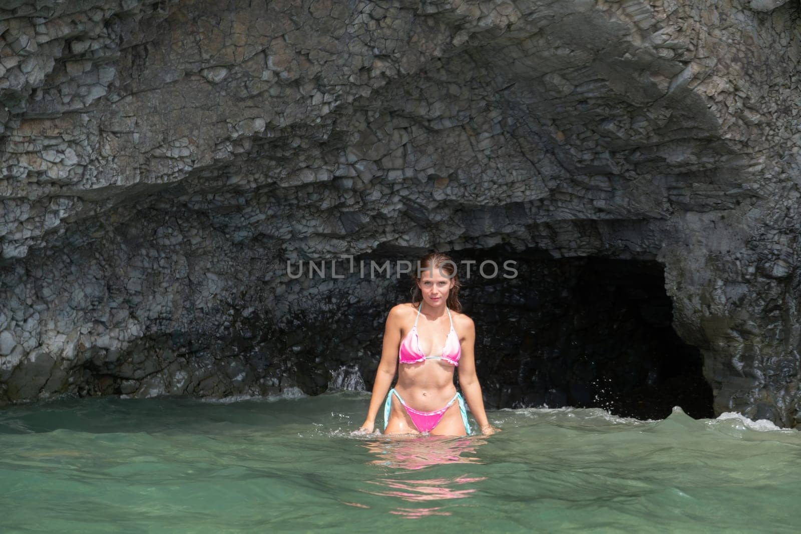 Woman travel sea. Happy Woman traveler shares adventure journey at sea, surrounded by volcanic mountains on beach. Happy tourist captures memory in pink bikini. by panophotograph