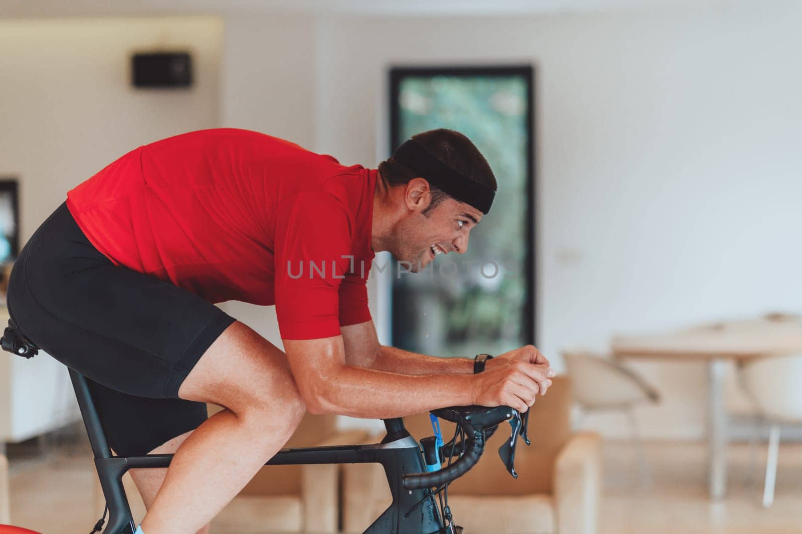 A man riding a triathlon bike on a machine simulation in a modern living room. Training during pandemic conditions