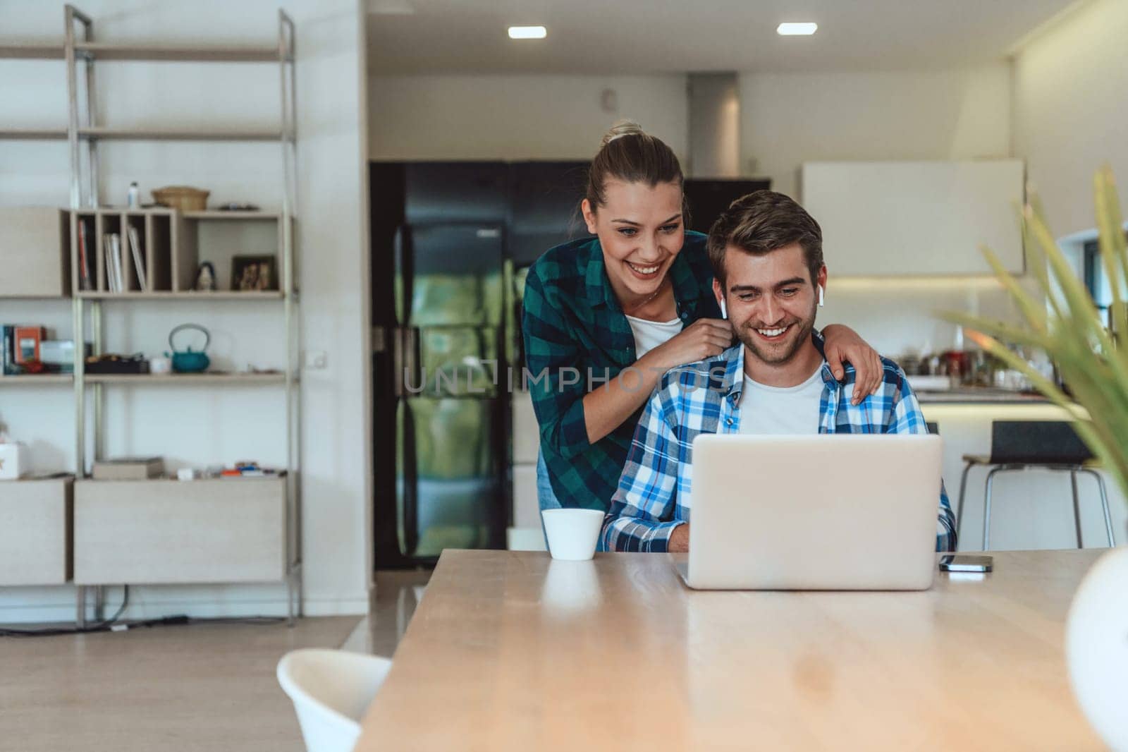 A young married couple is talking to parents, family and friends on a video call via a laptop while sitting in the living room of their modern house by dotshock