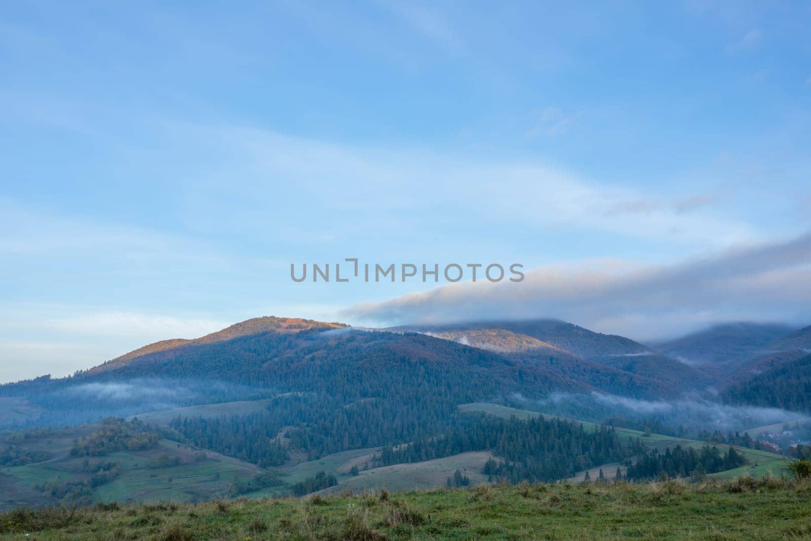 Early morning in summer Ukrainian Carpathians. Clouds over mountains and light fog between wooded hills