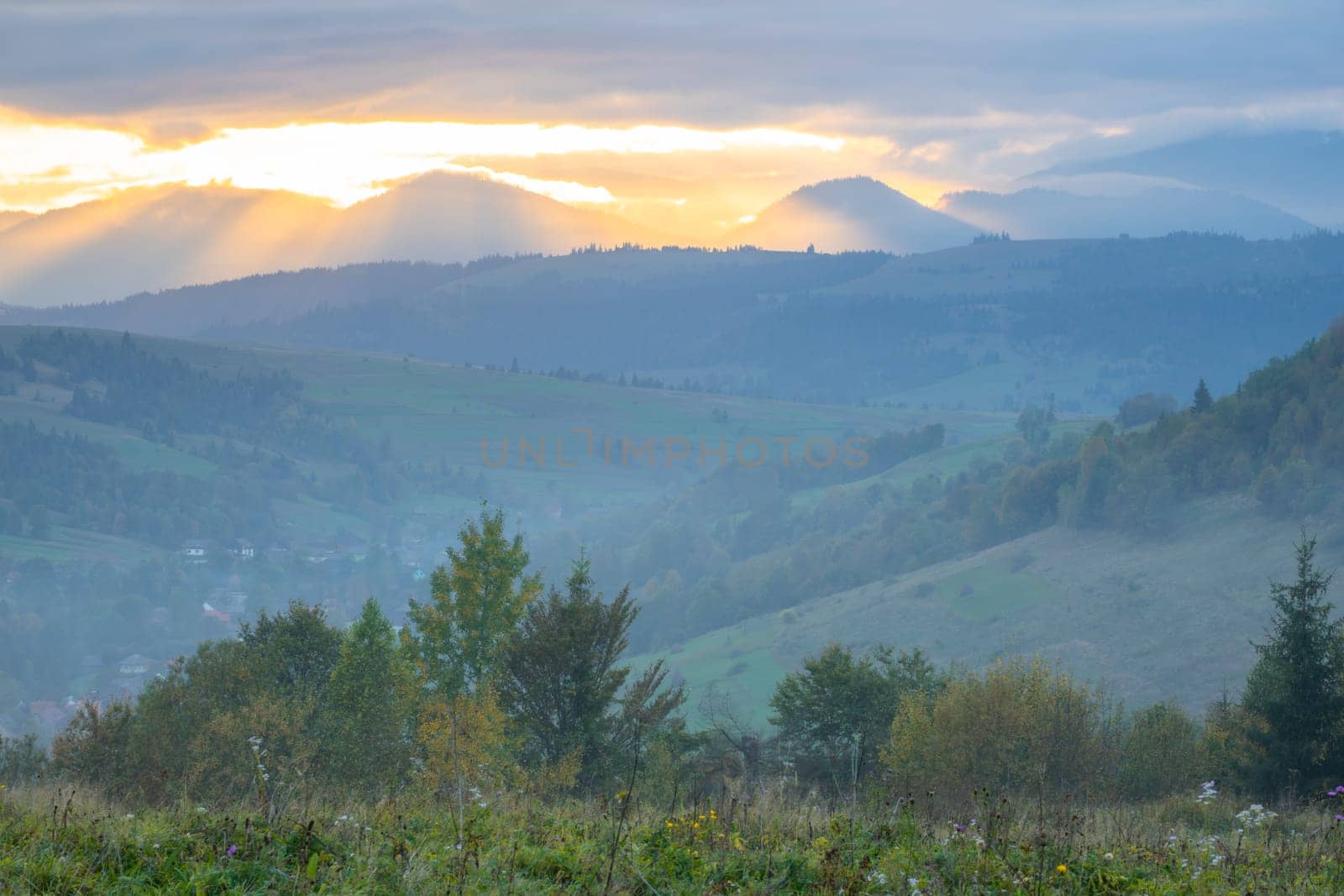 Summer evening in the Ukrainian Carpathians. Wooded mountains and small village. The last rays of the sun break through the dramatic clouds