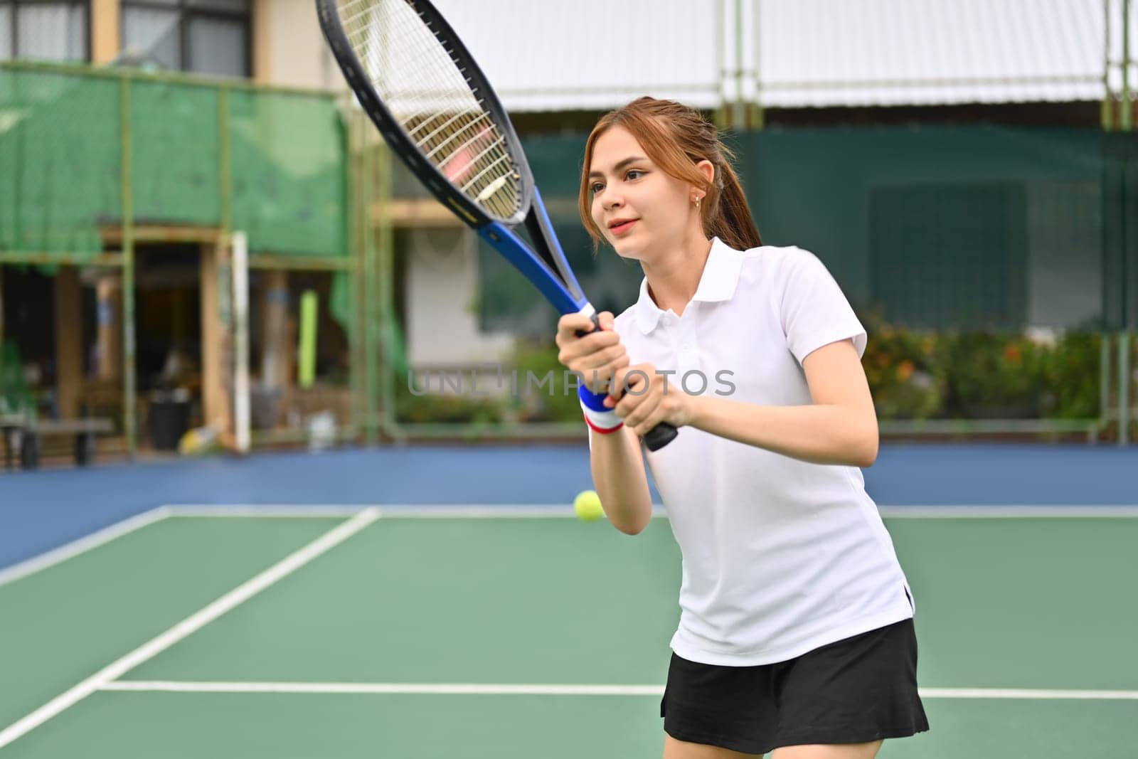 Joyful young woman hitting ball with racket to return ball over net. Sport, fitness, training and active life concept.