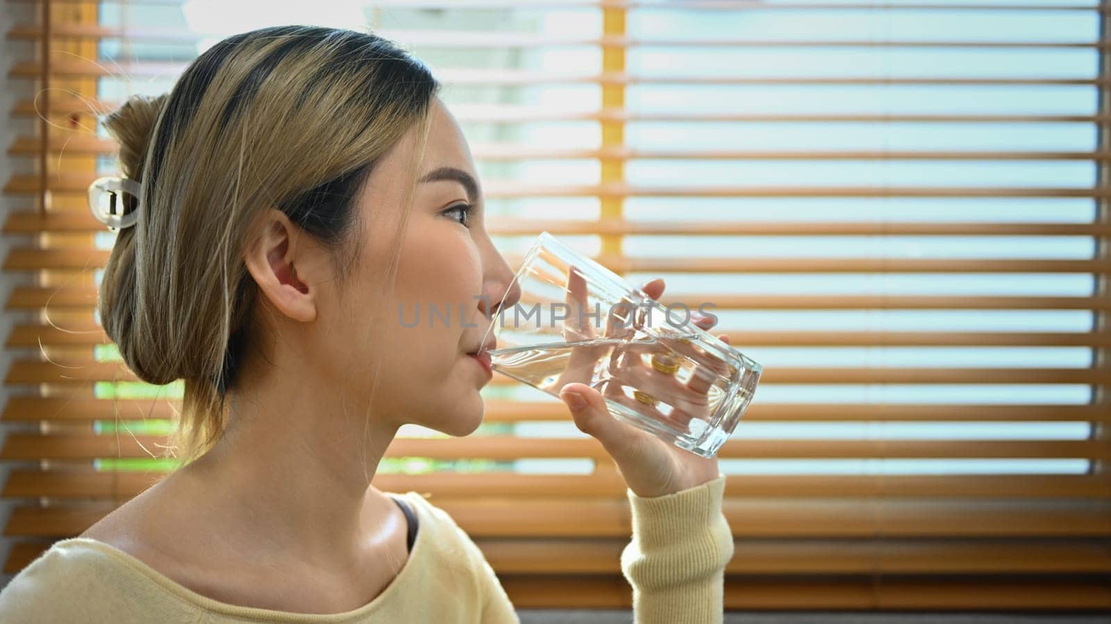 Beautiful young woman dressed in a casual wears drinking fresh mineral water from glass. Hydration and healthy lifestyle concept.