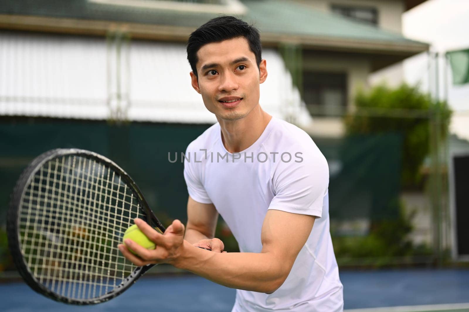 Focused asian male tennis player serving tennis ball during a match on open court. Sport, fitness, training and active life concept.