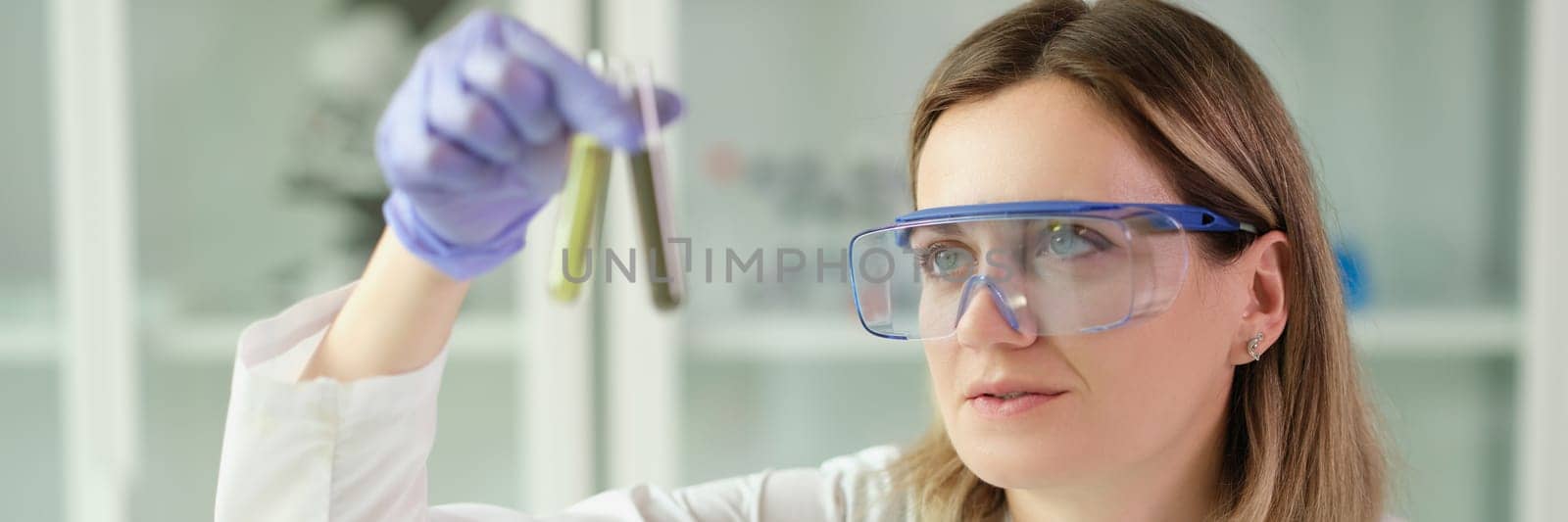 Woman chemist in protective glasses holding test tubes with liquid in hands in laboratory. Pharmaceutical business concept
