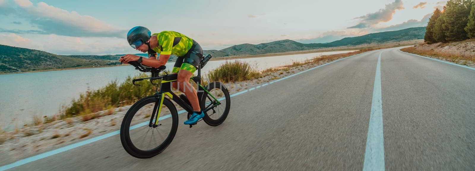 Full length portrait of an active triathlete in sportswear and with a protective helmet riding a bicycle. Selective focus.