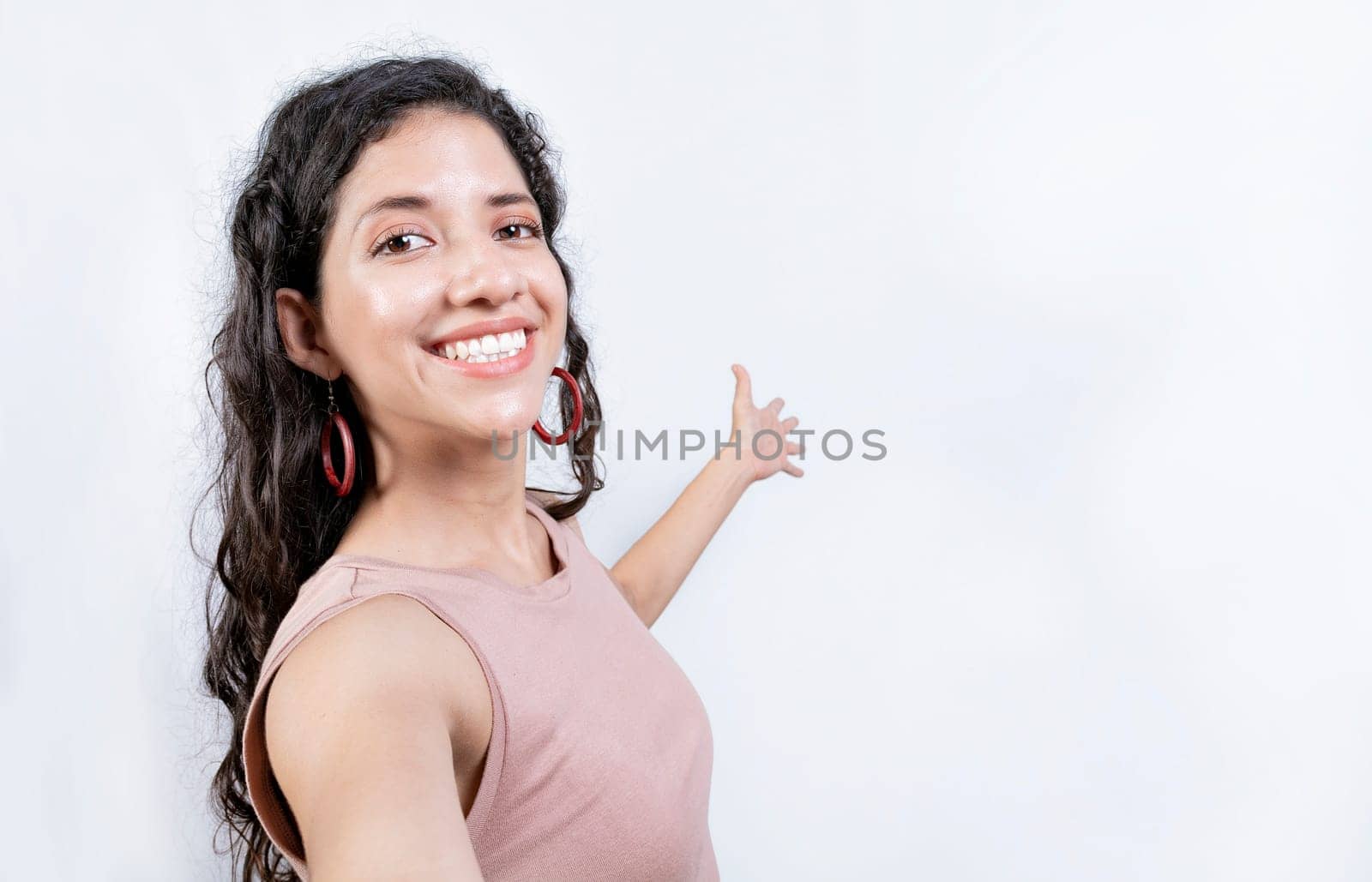 Happy Girl pointing back presenting a product. Young woman welcoming you isolated. Latin girl pointing a promotion with her palm by isaiphoto