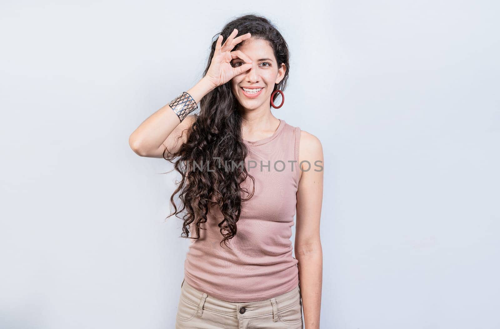 Happy young girl making ok gesture with hand looking through fingers. Friendly girl doing ok gesture looking through fingers by isaiphoto