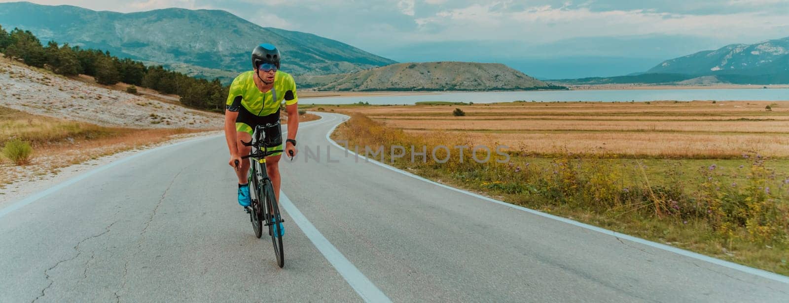 Full length portrait of an active triathlete in sportswear and with a protective helmet riding a bicycle. Selective focus.