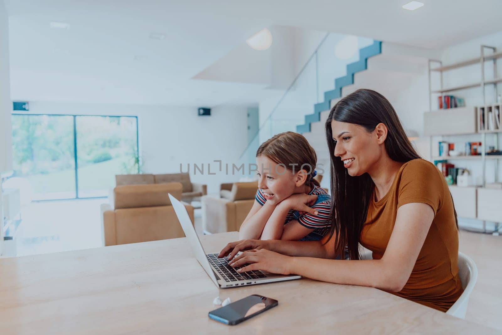 Mother with her daughter talking on laptop with family and friends while sitting in modern living room of big house by dotshock