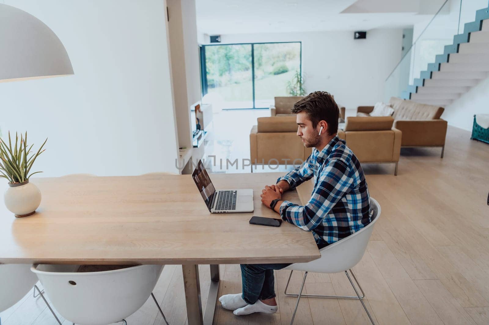 The man sitting at a table in a modern living room, with headphones using a laptop for business video chat, conversation with friends and entertainment.