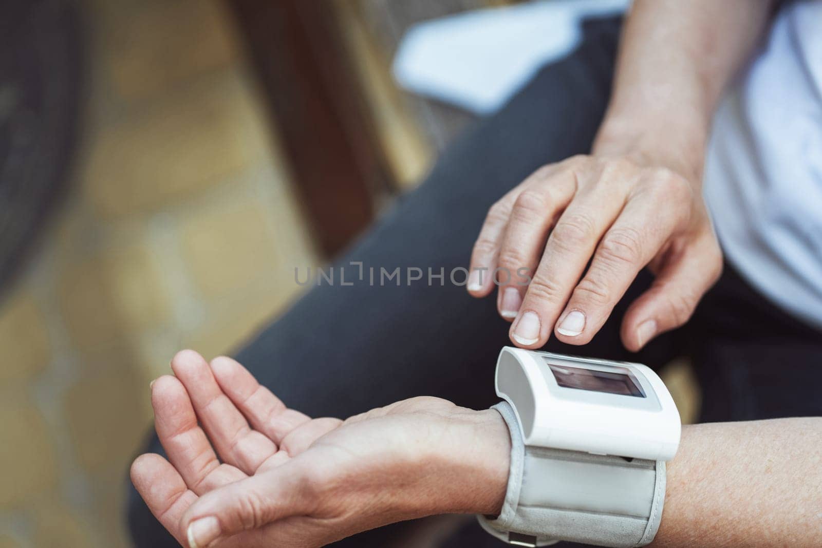 Old senior lady using pressure measuring apparatus to measure her blood pressure. Focus on hand, she carefully operates device outdoors. Regular health monitoring of seniors in maintaining well-being. High quality photo
