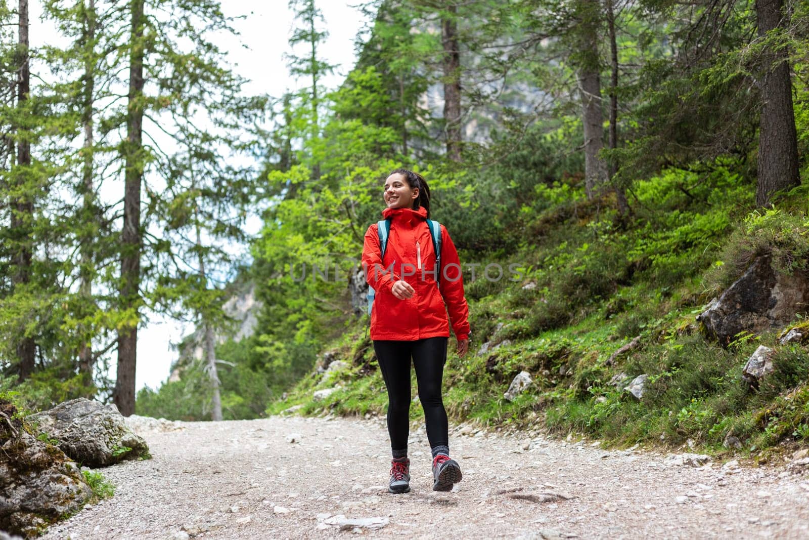 Fearless young woman hiking cheerfully alone in the mountain forest in a red raincoat looking towards the side.