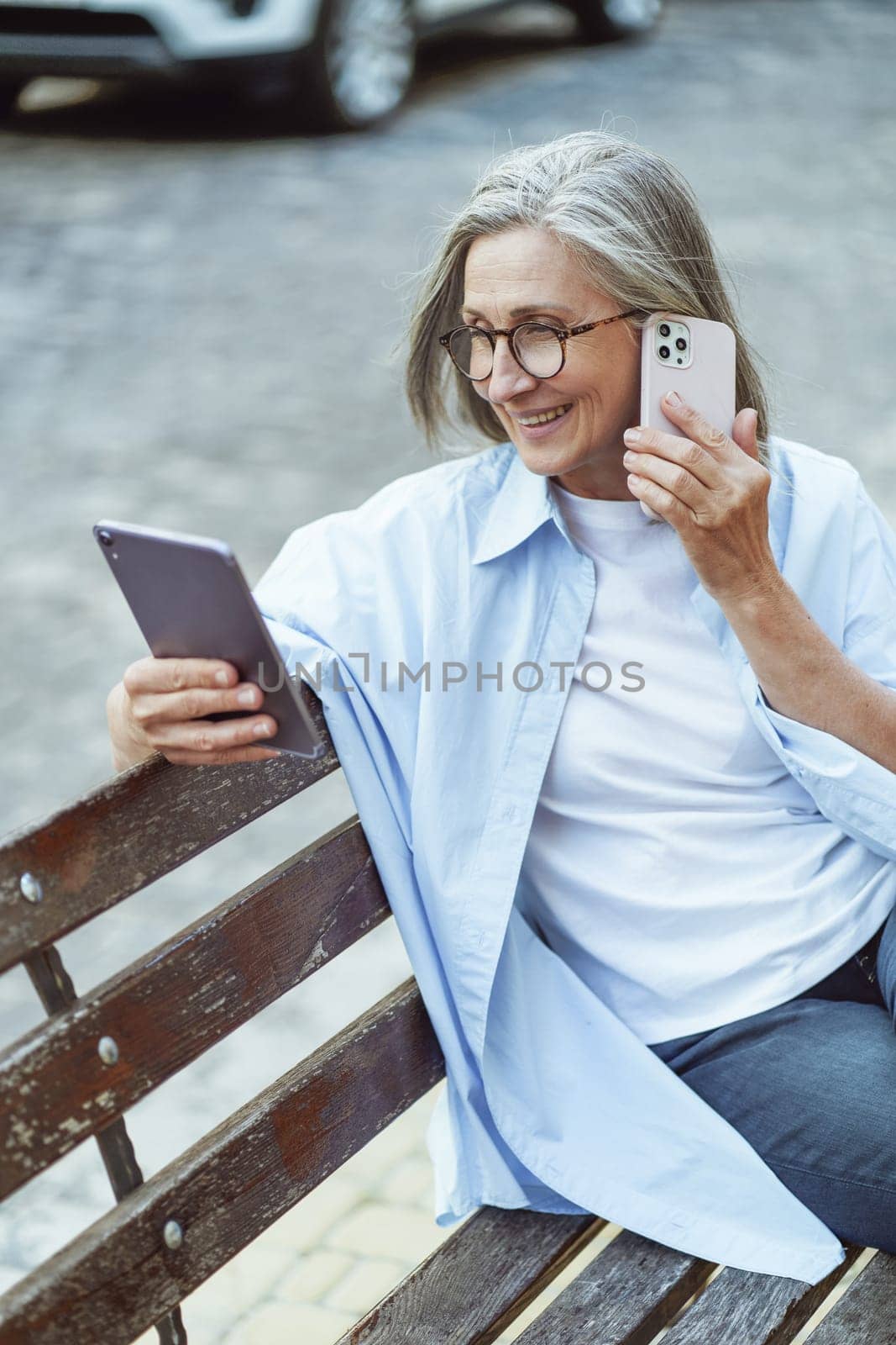 Senior woman searching for information online and speaking on mobile phone. Lady's use of technology to access information and maintain communication while enjoying ambiance of the historic city. . High quality photo