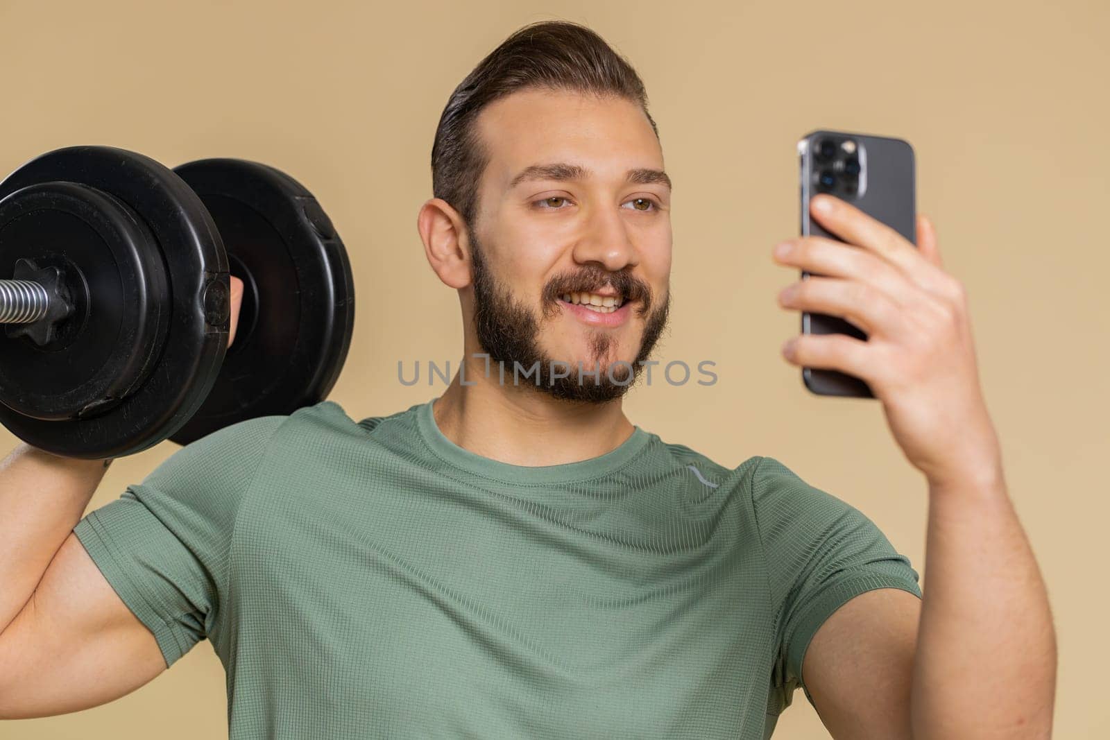 Athlete sportive man texting share messages content on smartphone social media applications online, sms message, browsing, reading news. Middle eastern sportsman guy with dumbbell on beige background