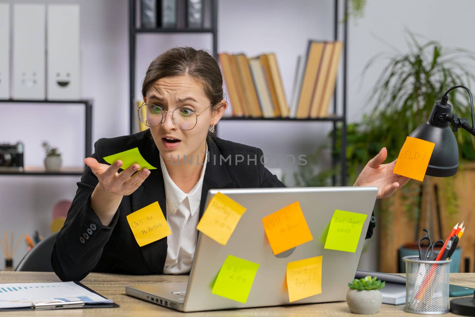 Tired exhausted young business woman working on laptop at office with many sticker task inscriptions. Freelancer girl busy occupation feels sad boredom overworked multitasking. Panic attack, deadline