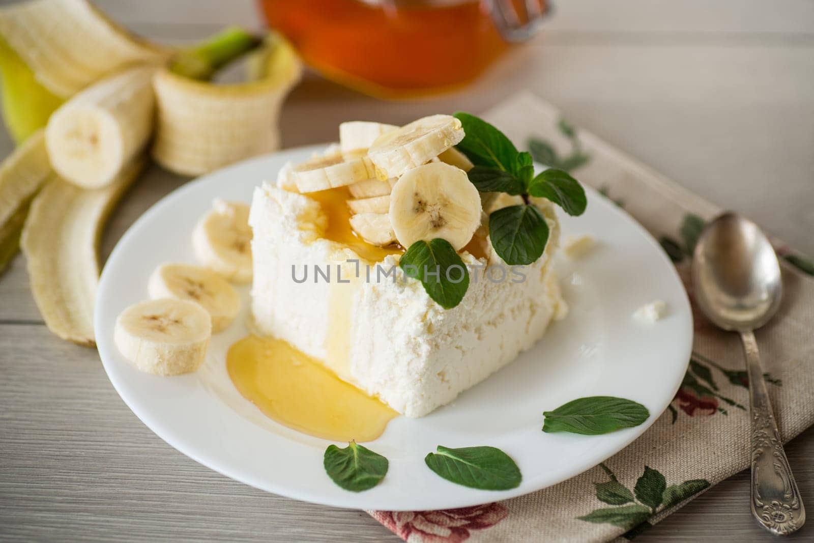 Portion of homemade milk curd with banana slices and honey, with mint in a plate.