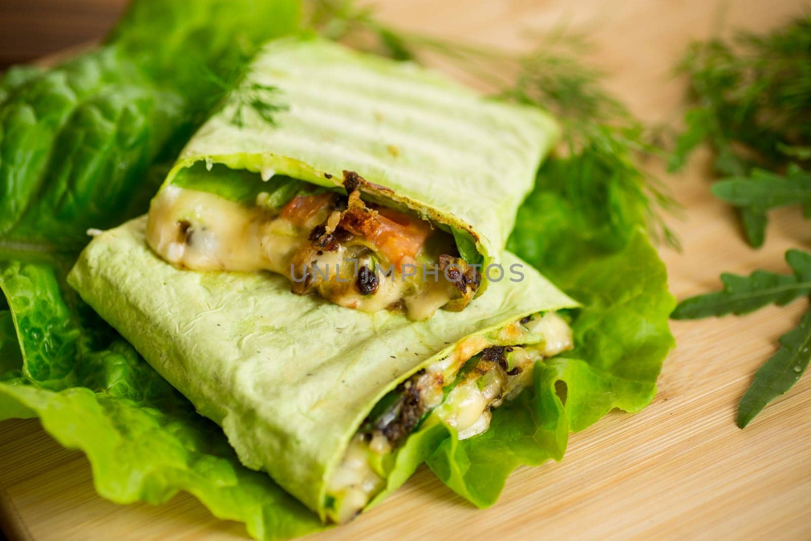 green hot vegetarian pita bread with mushrooms and different vegetables, with lettuce leaves on a wooden table.