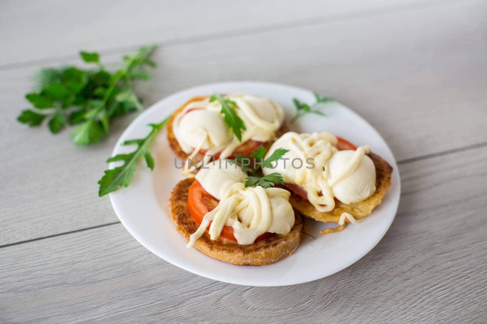 fried in batter sandwiches with tomatoes and mozzarella in a plate with herbs, on a wooden table.