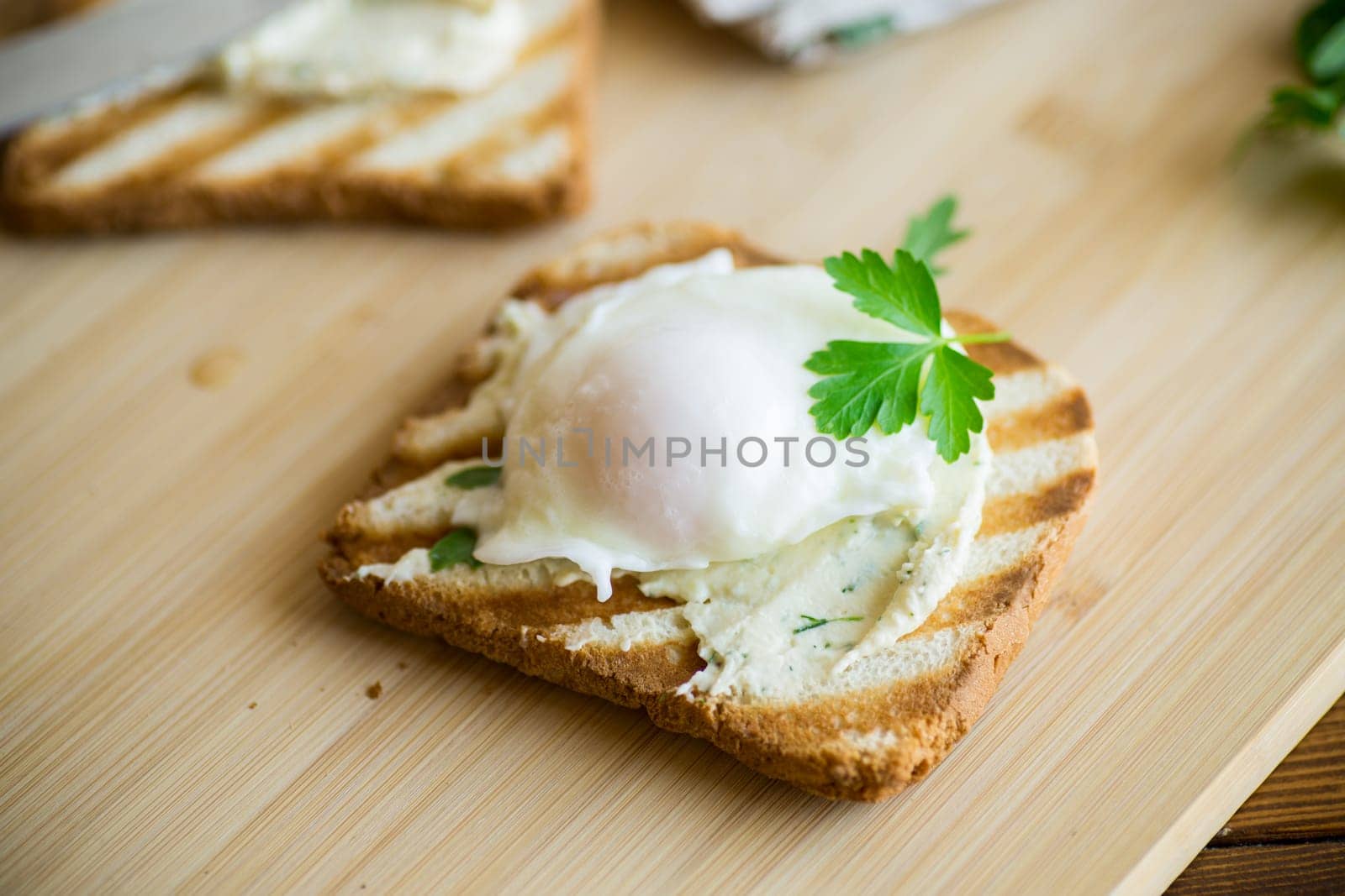 Fried toast bread with spread and poached egg, on a wooden table. Quick breakfast.