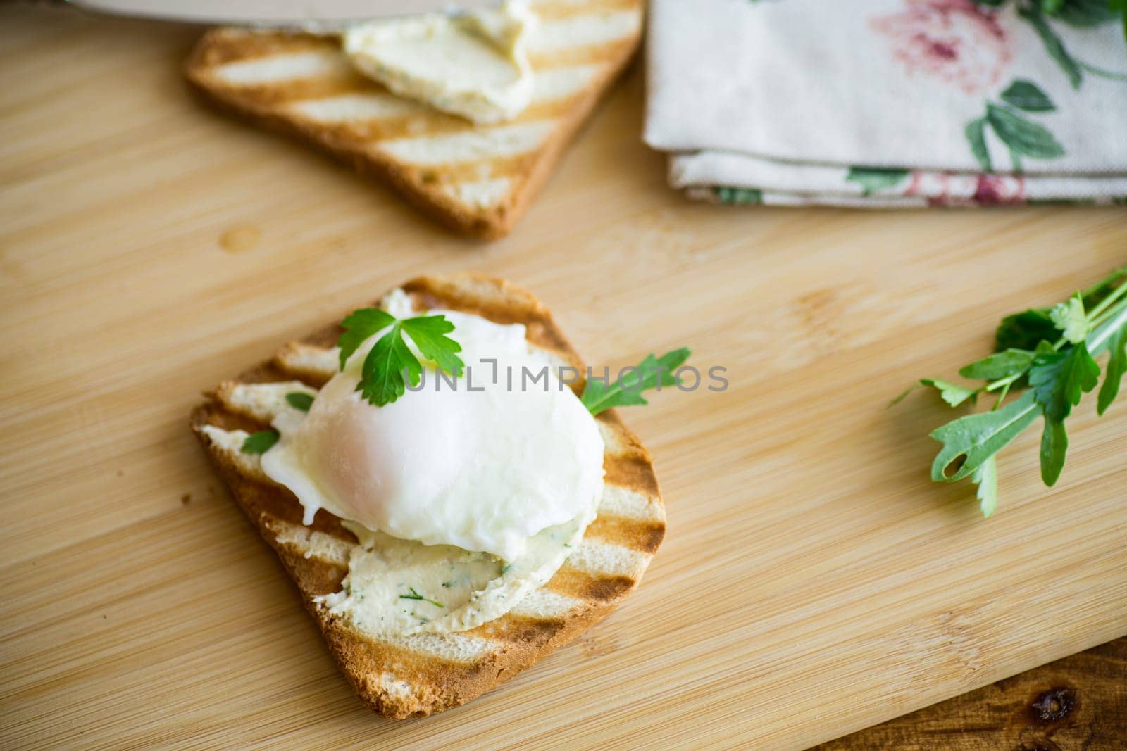 Fried toast bread with spread and poached egg, on a wooden table. Quick breakfast.