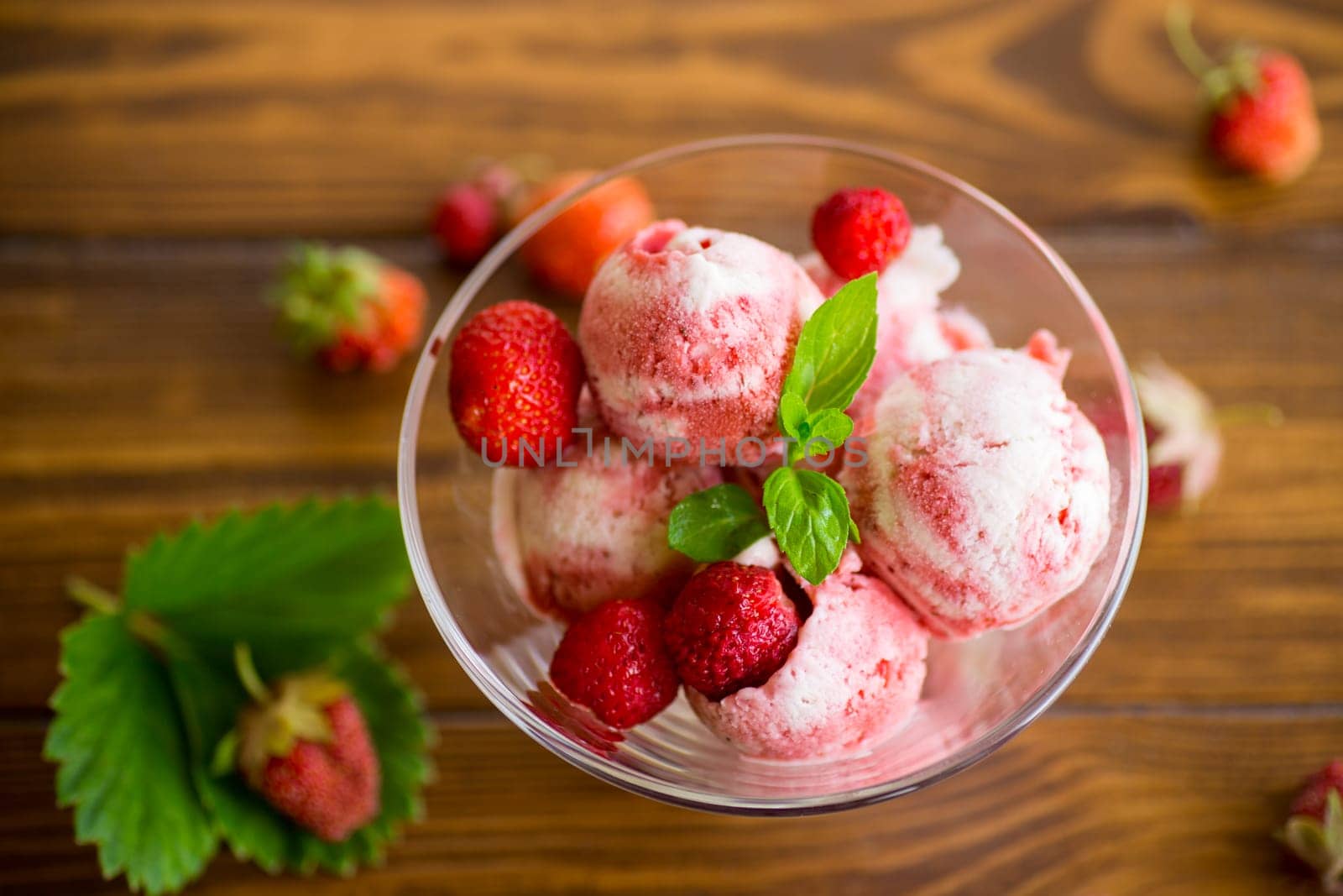 Balls of homemade strawberry ice cream in a bowl on a wooden table.