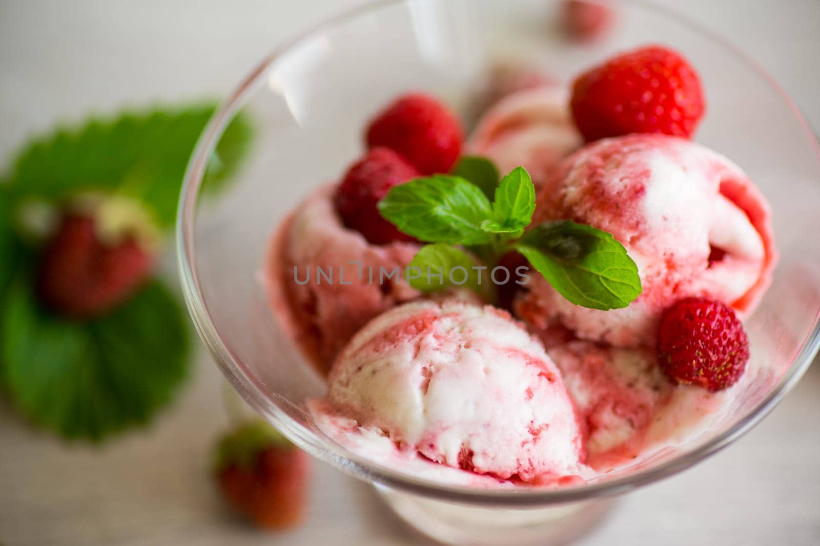 Balls of homemade strawberry ice cream in a bowl on a wooden table.