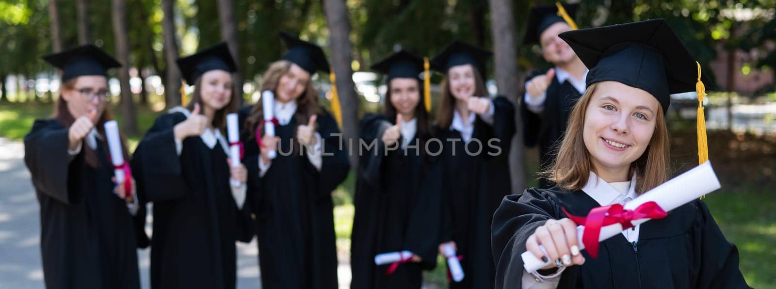 Happy young caucasian woman celebrating graduation with classmates. A group of graduate students outdoors. Widescreen
