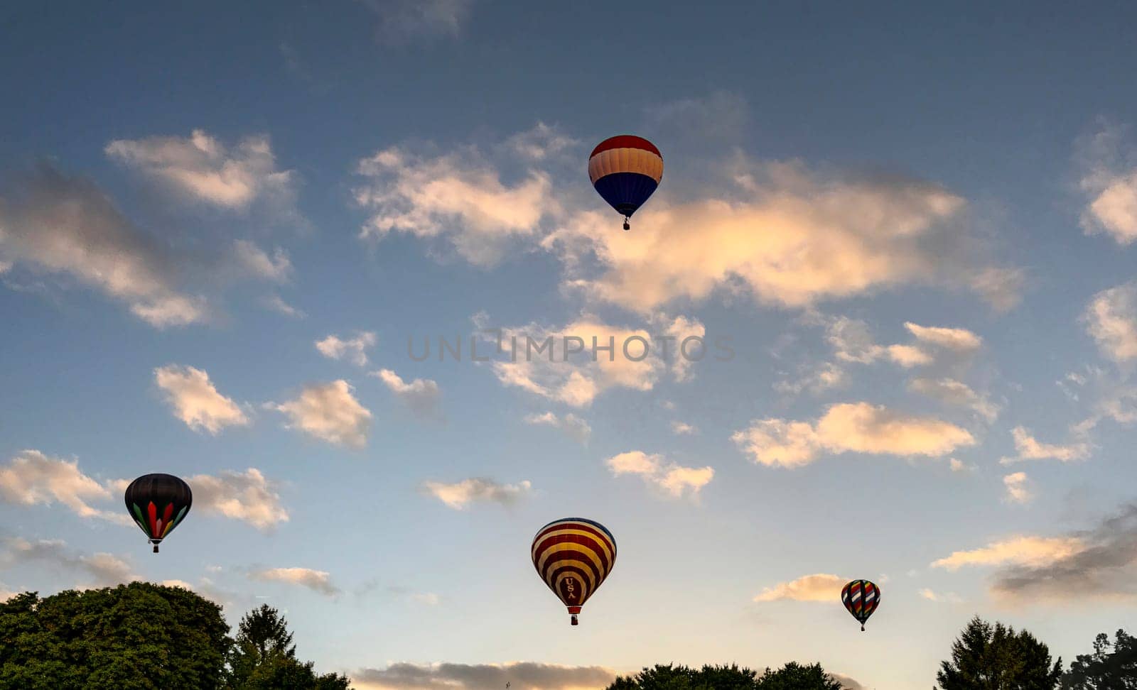 A View of Multiple Multi Colored Hot Air Balloons Floating in a Beautiful Morning Blue Sky With Thin Clouds