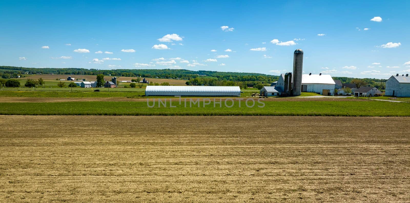 An Aerial View of a Plowed Field with a Barn, Silos and Farm House in View on a Spring Day