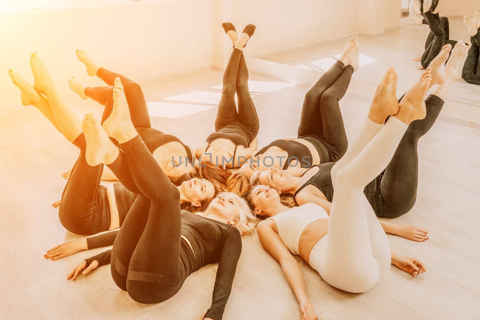 Group of young womans fitness instructor in Sportswear Leggings and Tops, stretching in the gym before pilates, on a yoga mat near the large window on a sunny day, female fitness yoga routine concept.