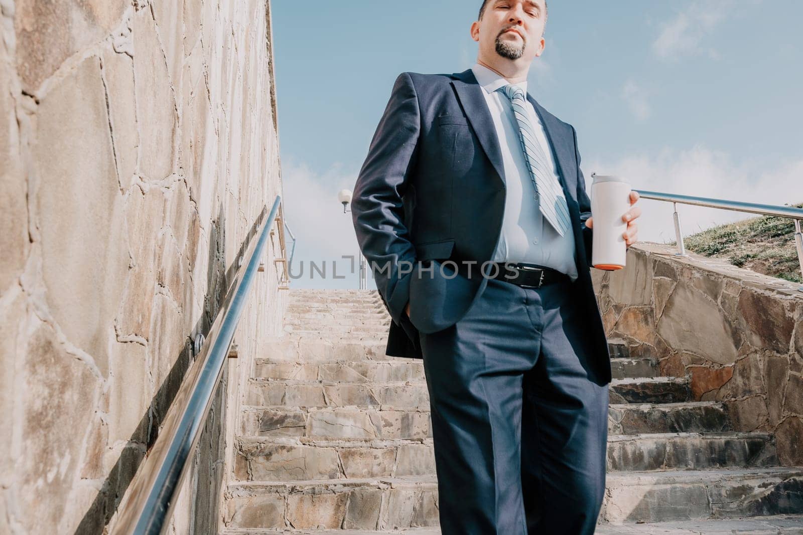 Confident middle age businessman with briefcase walking upstairs. Close-up of businessman wearing blue suit holding bag walking down the stairs by panophotograph