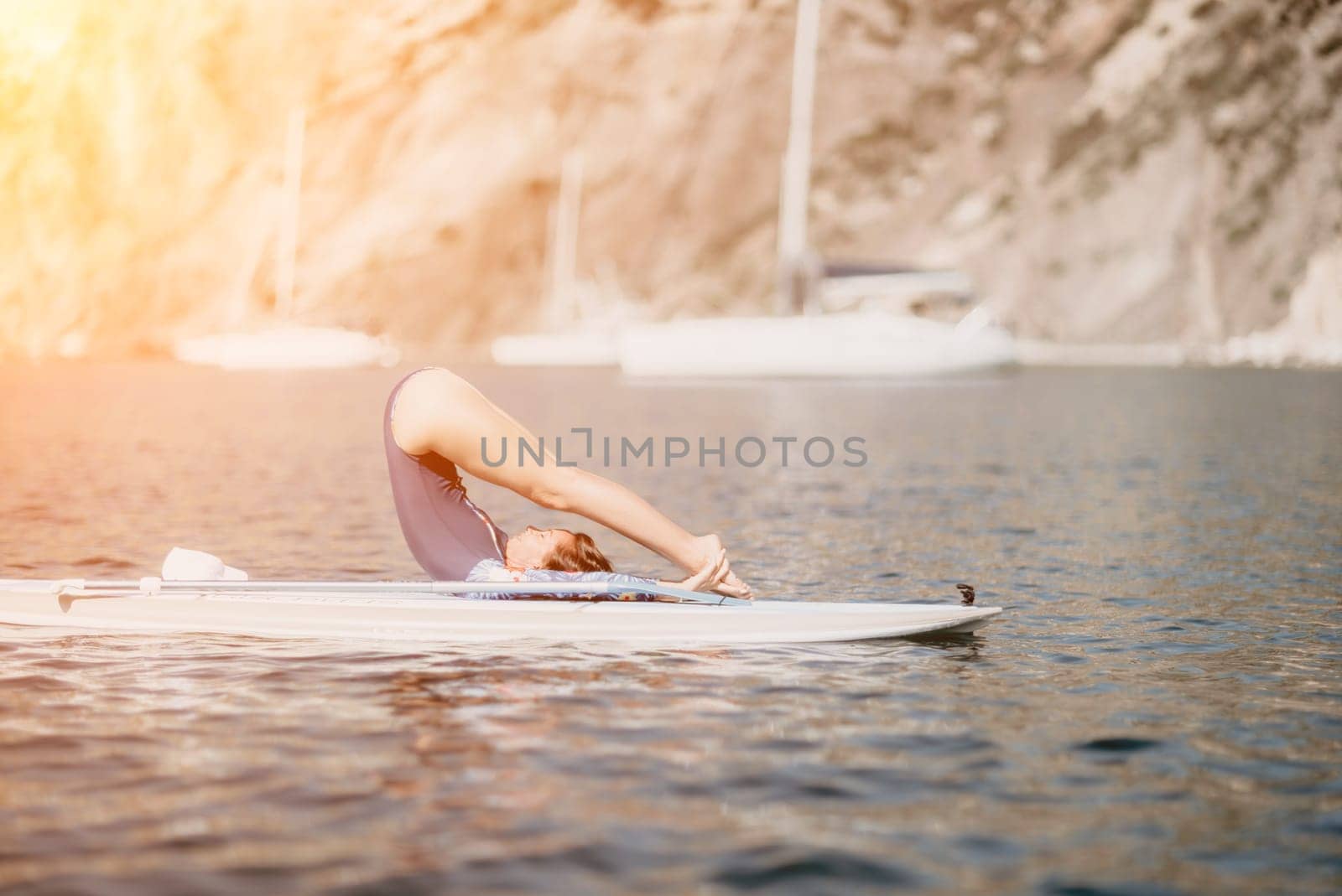 Woman sup yoga. Middle age sporty woman practising yoga pilates on paddle sup surfboard. Female stretching doing workout on sea water. Modern individual female hipster outdoor summer sport activity. by panophotograph