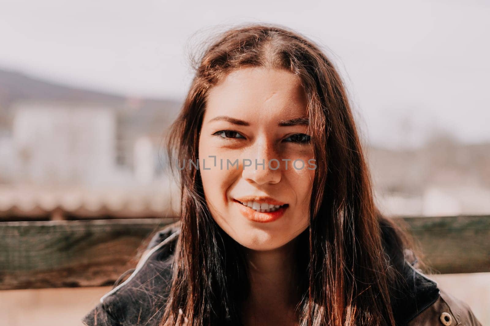 Happy young smiling woman with freckles outdoors portrait. Soft sunny colors. Outdoor close-up portrait of a young brunette woman and looking to the camera, posing against autumn nature background by panophotograph