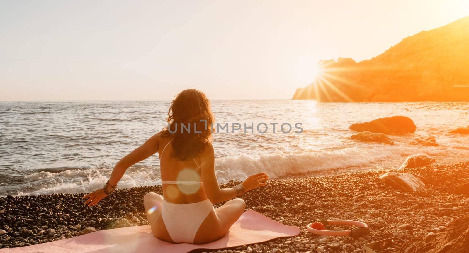 Woman sea yoga. Happy woman in white swimsuit and boho style braclets practicing outdoors on yoga mat by sea on sunset. Women yoga fitness routine. Healthy lifestyle, harmony and meditation by panophotograph