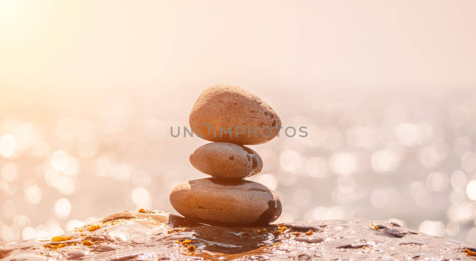 Balanced Pebbles Pyramid on the Beach on Sunny Day and Clear Sky at Sunset. Blue Sea on Background Selective focus, zen stones on sea beach, meditation, spa, harmony, calm, balance concept.