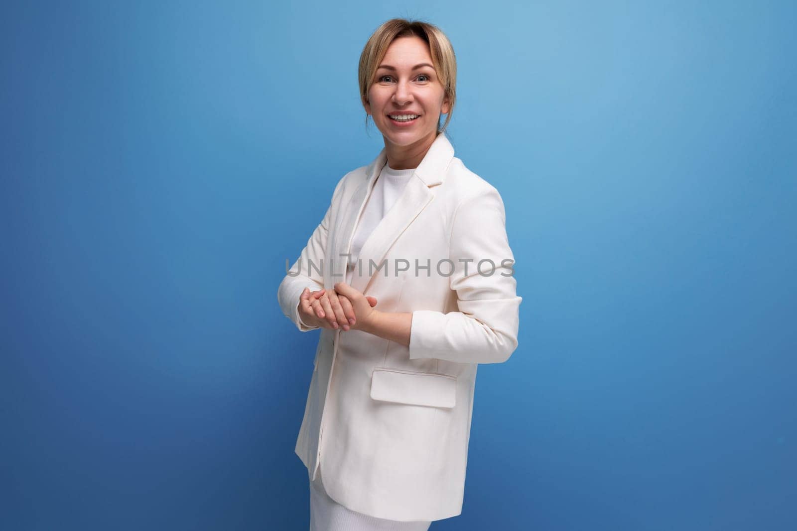 young slim blond business woman in a white elegant jacket and skirt on a blue background with copy space.