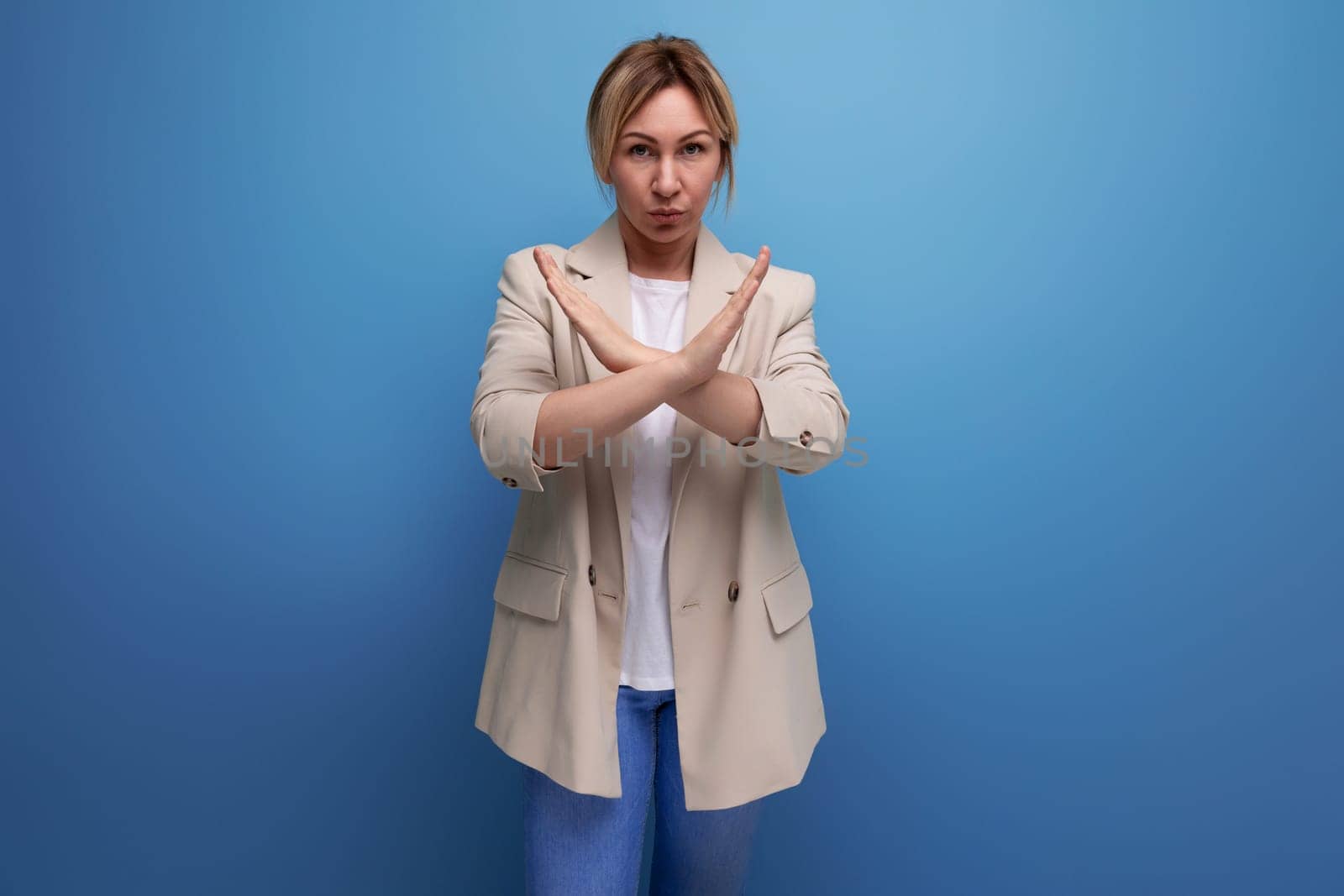 blond young business woman in jacket with arms crossed on studio background.