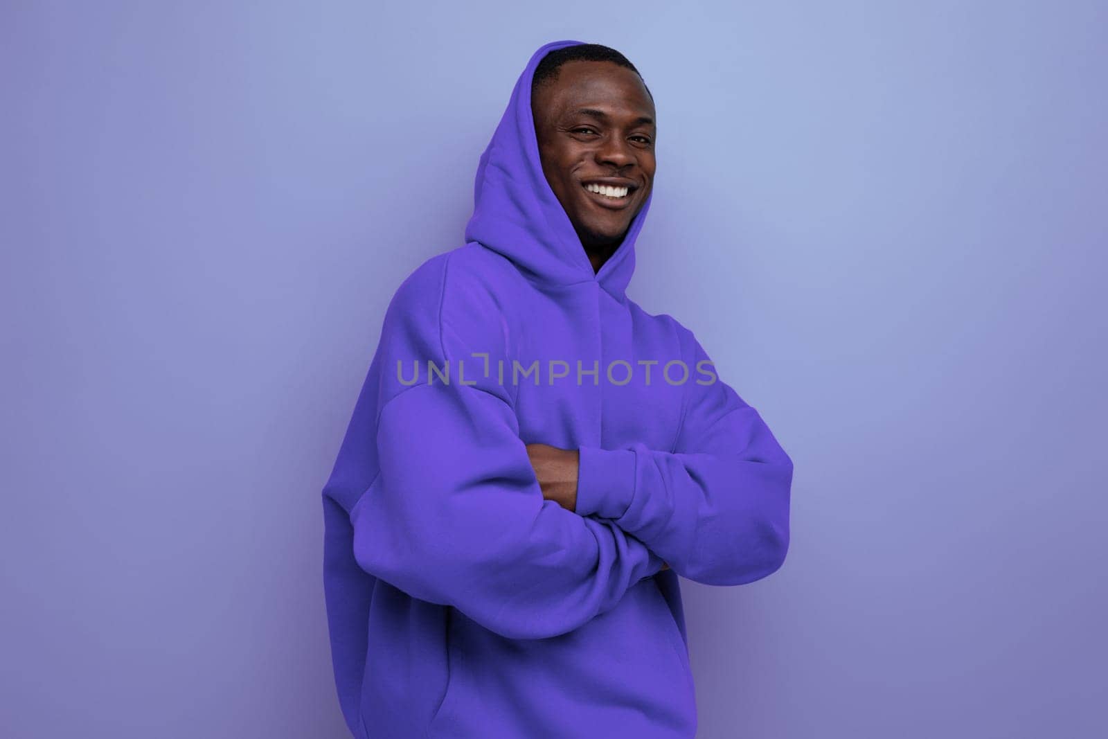 cheerful cute ethnic 25 year old african man in a stylish hoodie with a hood on a blue background.