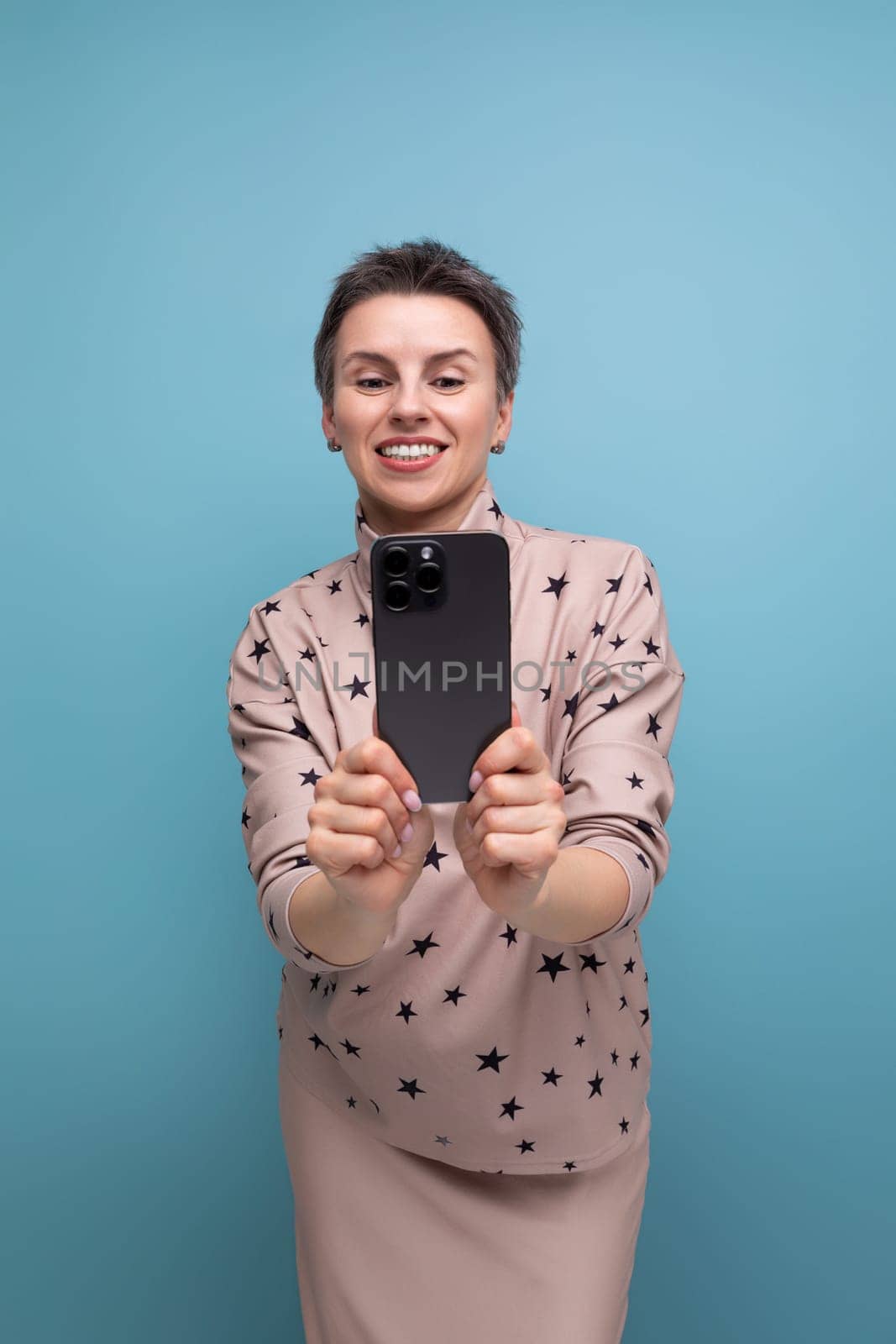 successful young career woman with gray streaked hair dressed in a skirt and blouse takes a photo on a smartphone by TRMK