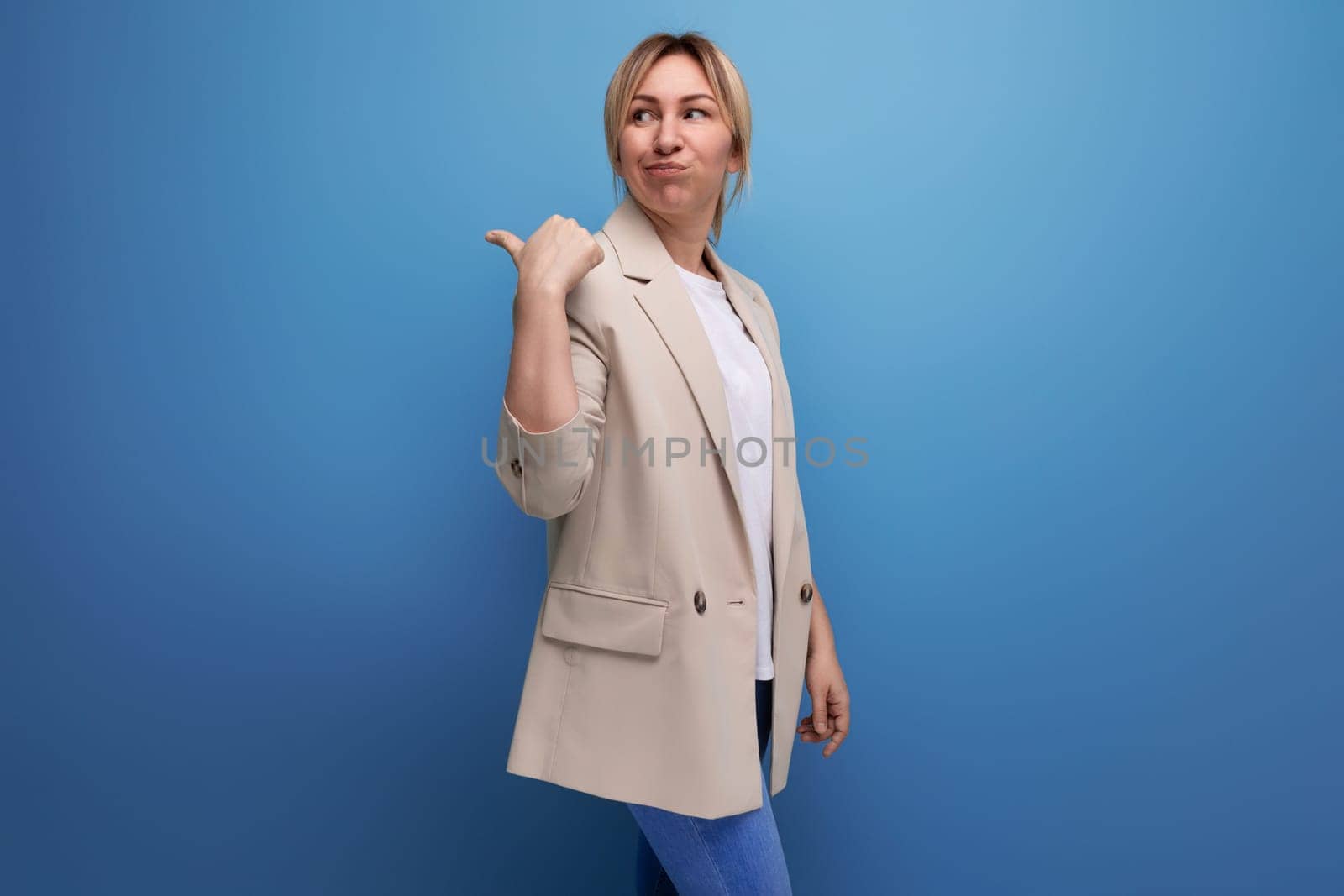 close-up of a blonde woman in an office jacket standing thoughtfully on a blue background with copy space by TRMK