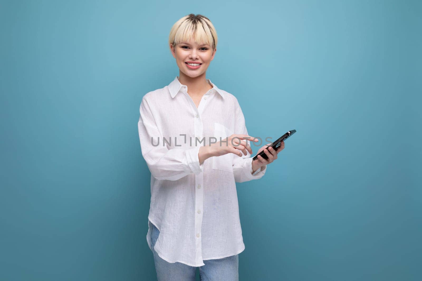 well-groomed cute blond fashionable woman with a short haircut dressed in a white shirt is typing a message on the phone.