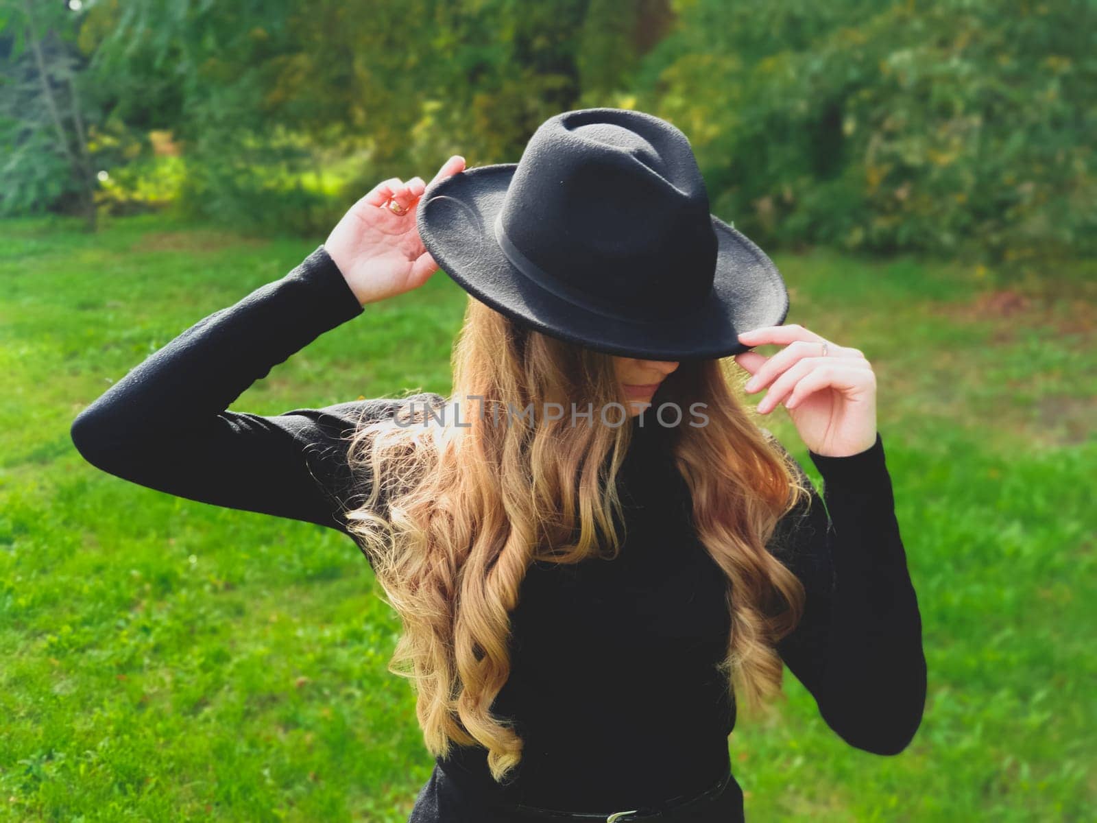 Outdoor lifestyle fashion photo of young natural beautiful lady in park with black hat and sweater. Warm Autumn.