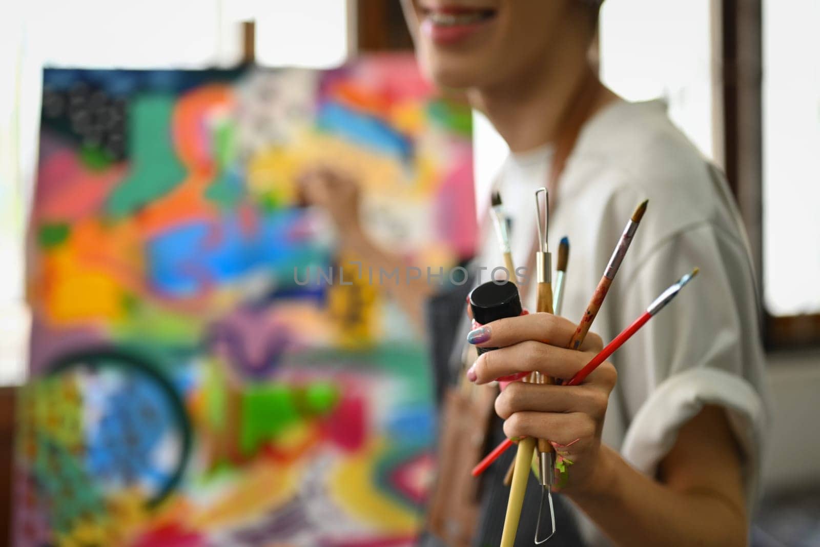 Select focus on hand of artist holding paintbrushes standing in art studio. Art, hobby and leisure activity concept.