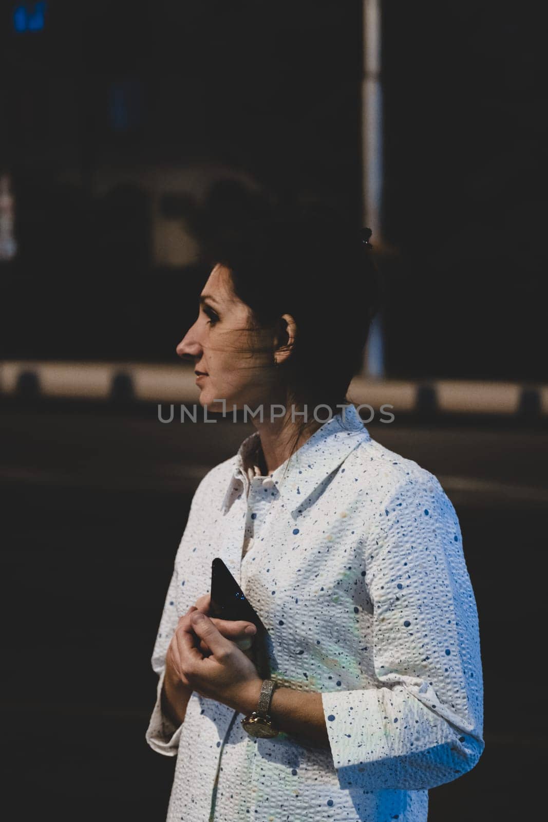 Outdoor portrait of beautiful young woman holding her mobile phone at night. Fashion