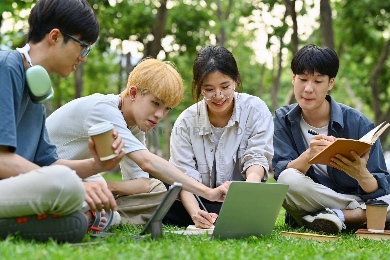 Gen Z friends university students reading book, working on group project at campus. Education and youth lifestyle concept.